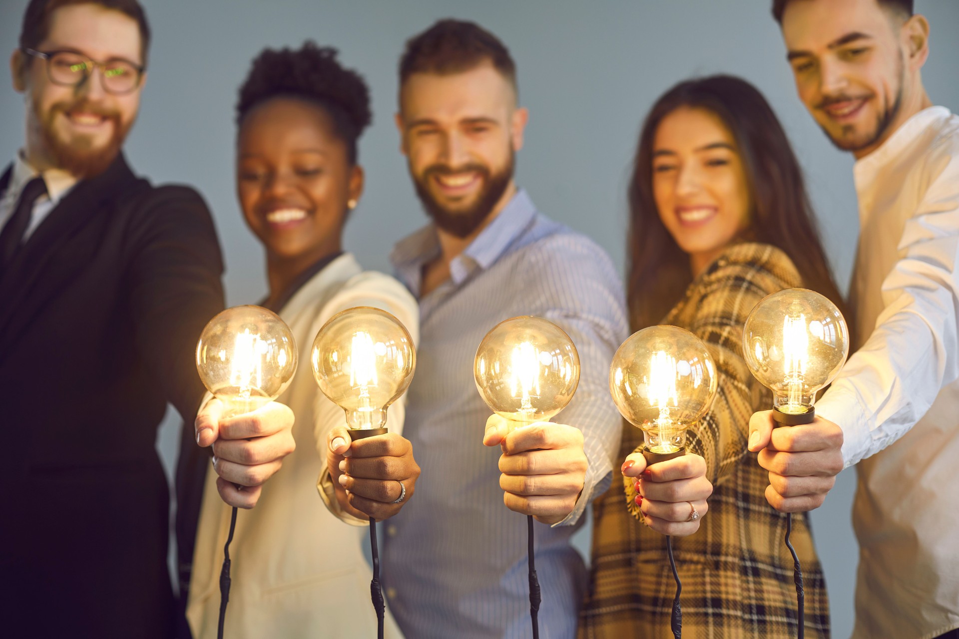 Group of happy creative young diverse business people holding shining light bulbs